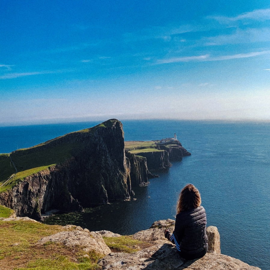ragazza seduta di spalle che guarda Neist Point in Scozia